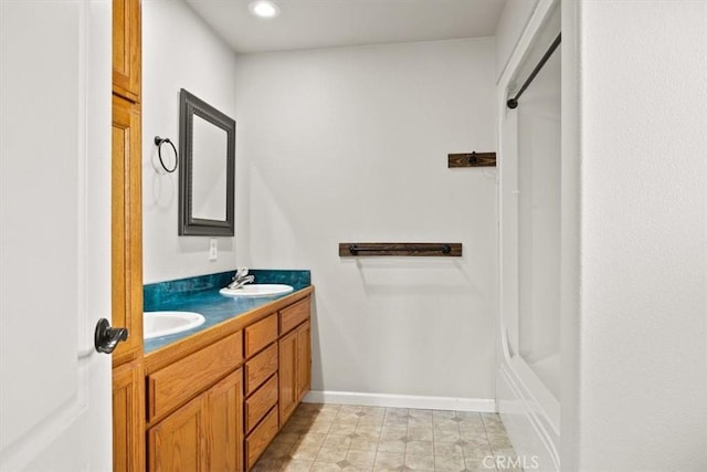 bathroom with a sink, baseboards, a shower, and double vanity