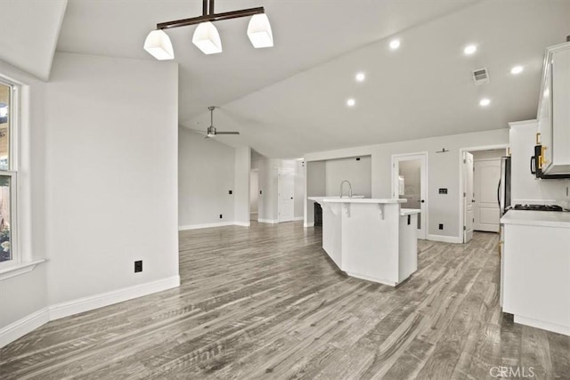 kitchen with lofted ceiling, white cabinetry, an island with sink, ceiling fan, and a breakfast bar