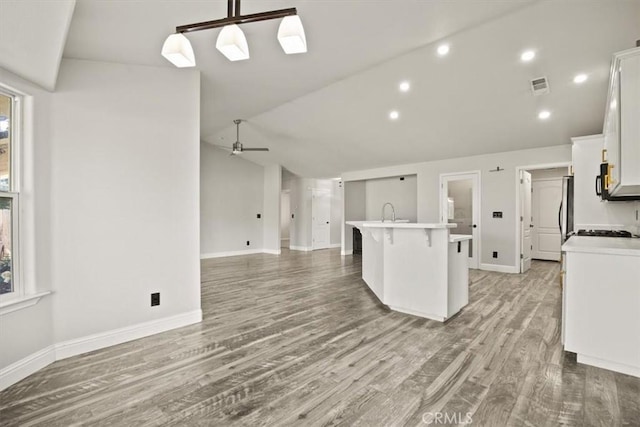 kitchen with a breakfast bar, a center island with sink, white cabinetry, light wood-style floors, and vaulted ceiling