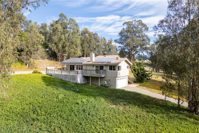 rear view of property featuring a lawn, a garage, and solar panels