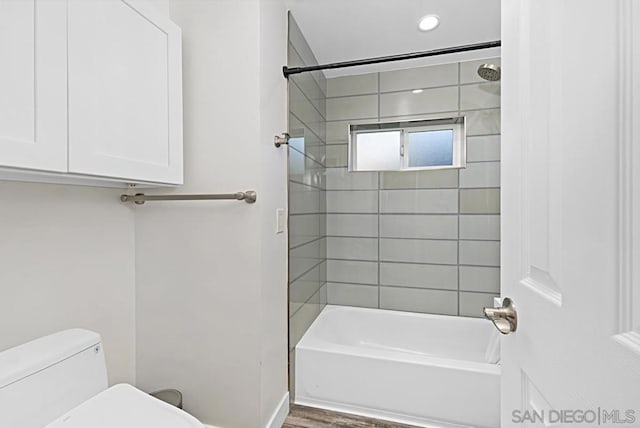 bathroom with hardwood / wood-style floors, tiled shower / bath combo, and toilet