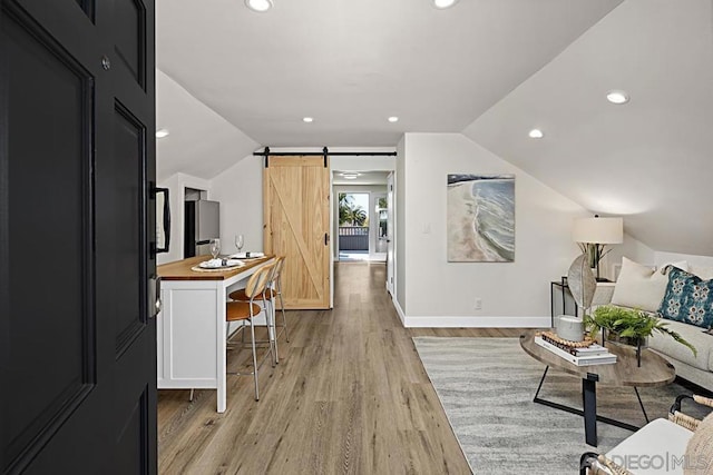 living room featuring a barn door, vaulted ceiling, and light wood-type flooring