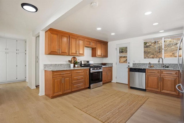 kitchen featuring light stone countertops, stainless steel appliances, light hardwood / wood-style flooring, and sink