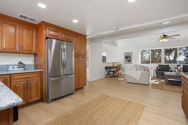 kitchen with ceiling fan, stainless steel fridge, light stone counters, and light hardwood / wood-style floors