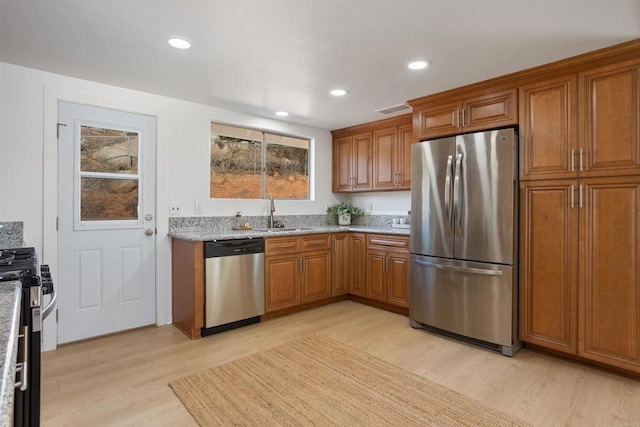 kitchen with light stone countertops, sink, stainless steel appliances, and light wood-type flooring