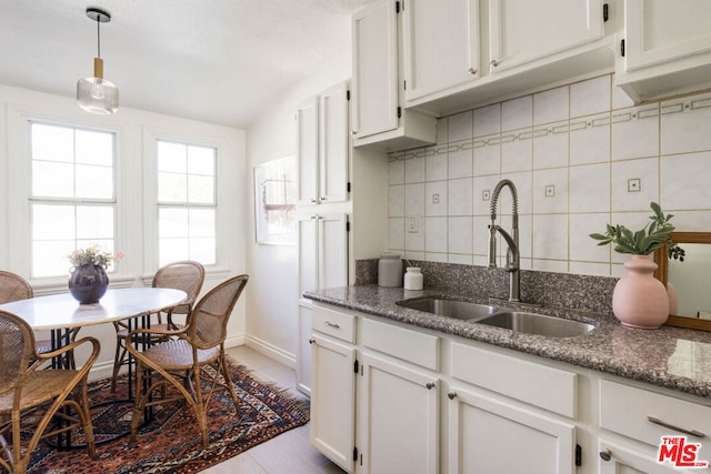 kitchen featuring white cabinets, pendant lighting, sink, and dark stone counters