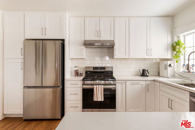 kitchen featuring sink, backsplash, appliances with stainless steel finishes, white cabinets, and light wood-type flooring