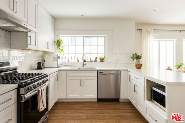 kitchen with white cabinets, appliances with stainless steel finishes, dark hardwood / wood-style flooring, and kitchen peninsula