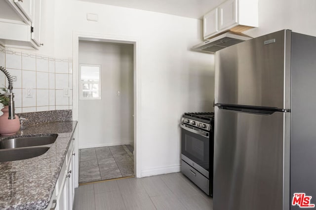 kitchen with dark stone counters, stainless steel appliances, sink, white cabinetry, and range hood