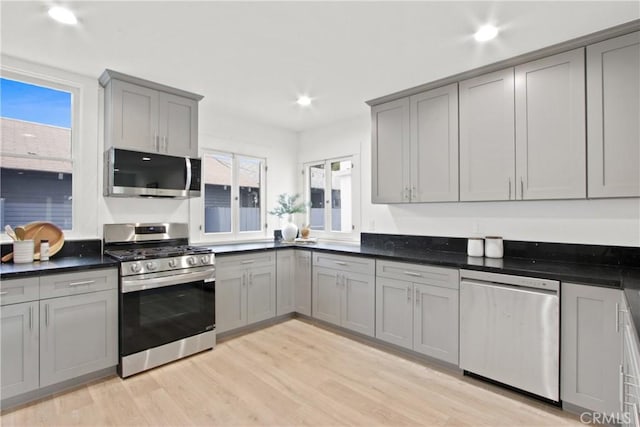 kitchen with gray cabinets, dark stone countertops, light wood-type flooring, and appliances with stainless steel finishes