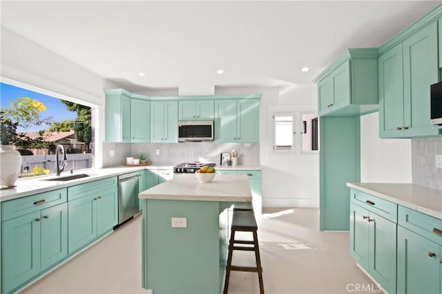 kitchen with a center island, backsplash, sink, light stone countertops, and appliances with stainless steel finishes