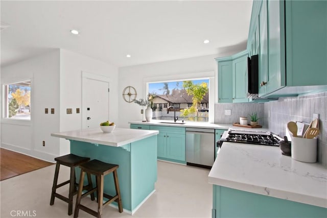 kitchen with sink, a center island, light stone counters, decorative backsplash, and appliances with stainless steel finishes