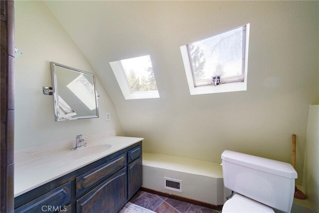 bathroom with toilet, vanity, lofted ceiling with skylight, and tile patterned floors