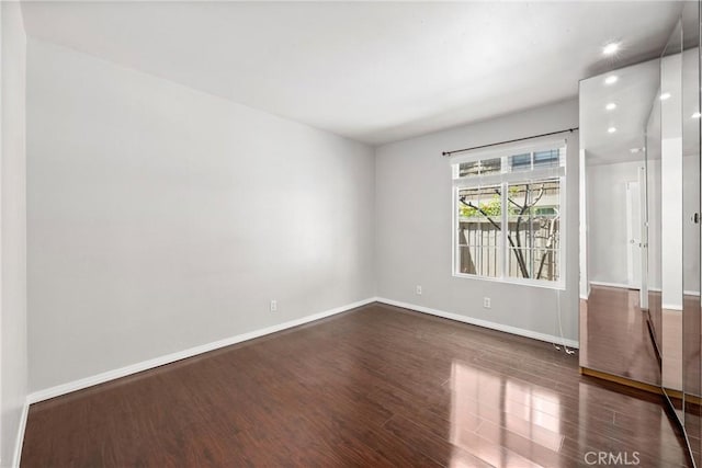 empty room with dark wood-style flooring, recessed lighting, and baseboards