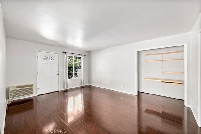 interior space featuring dark wood-style flooring, a wall unit AC, and baseboards