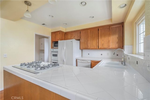 kitchen with sink, kitchen peninsula, tile countertops, decorative light fixtures, and white appliances