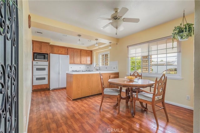 kitchen with kitchen peninsula, wood-type flooring, white appliances, and ceiling fan