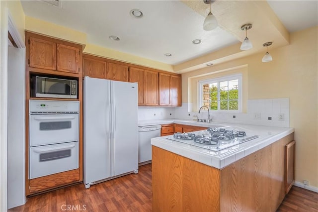 kitchen with hanging light fixtures, dark hardwood / wood-style floors, kitchen peninsula, white appliances, and decorative backsplash