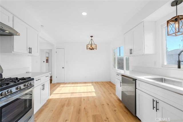 kitchen with white cabinets, light hardwood / wood-style floors, decorative light fixtures, and appliances with stainless steel finishes