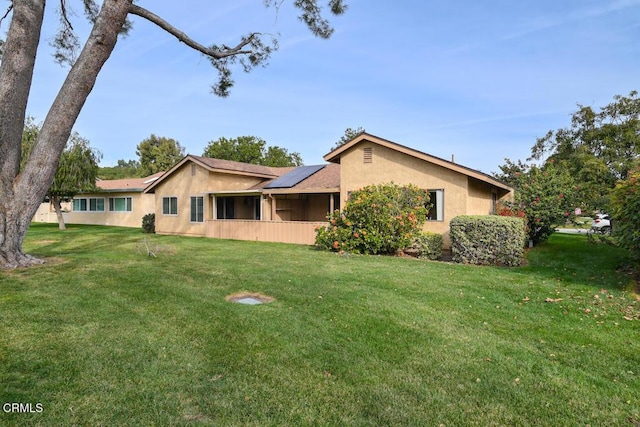 rear view of property with a lawn and solar panels