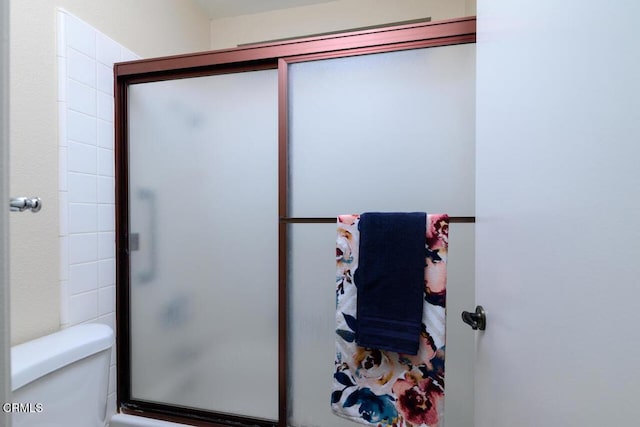 bathroom featuring a shower with door and toilet