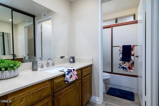 full bathroom with hardwood / wood-style floors, vanity, toilet, and bath / shower combo with glass door