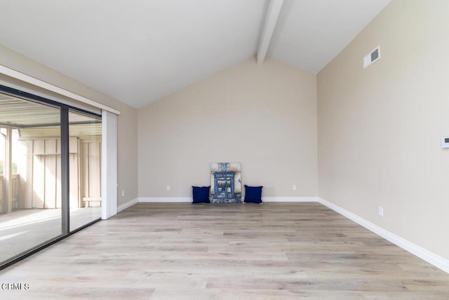 empty room featuring lofted ceiling with beams and light wood-type flooring