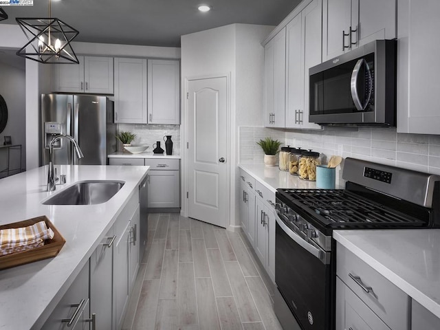 kitchen featuring tasteful backsplash, gray cabinetry, stainless steel appliances, sink, and pendant lighting