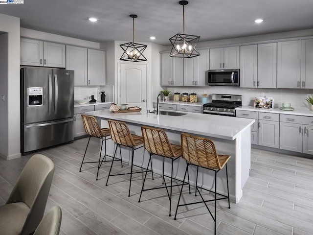 kitchen with sink, stainless steel appliances, light hardwood / wood-style floors, decorative light fixtures, and a center island with sink