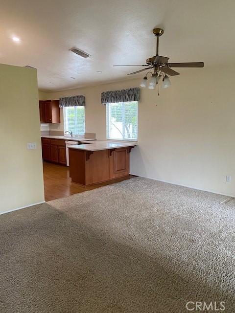 kitchen featuring dishwasher, light colored carpet, kitchen peninsula, and ceiling fan