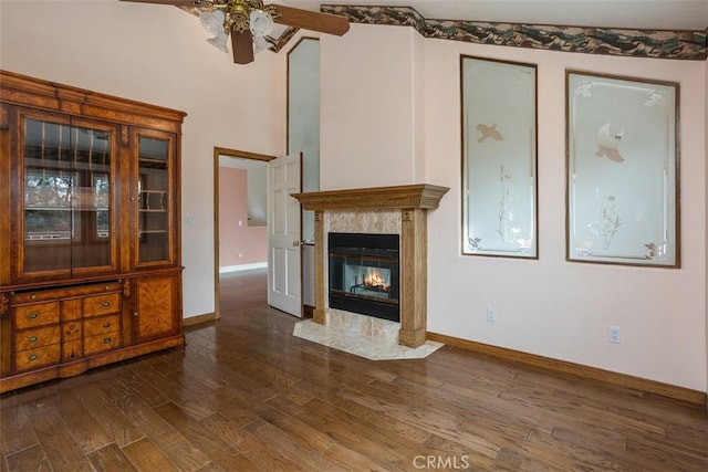 unfurnished living room with ceiling fan, a premium fireplace, and dark wood-type flooring