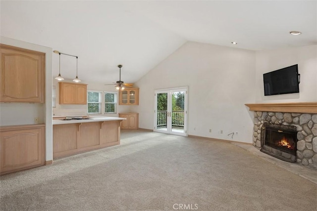 kitchen featuring light carpet, light brown cabinetry, ceiling fan, decorative light fixtures, and a stone fireplace