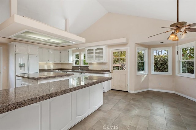 kitchen featuring vaulted ceiling, ceiling fan, white refrigerator with ice dispenser, dark stone countertops, and white cabinets