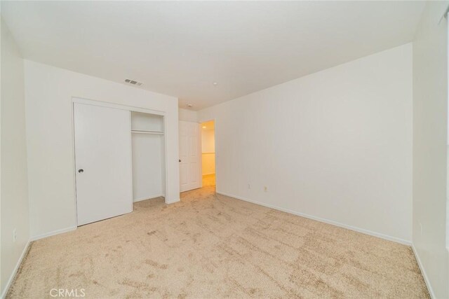 unfurnished bedroom with a closet and light colored carpet