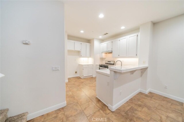 kitchen with a kitchen bar, stainless steel range, white cabinetry, and kitchen peninsula