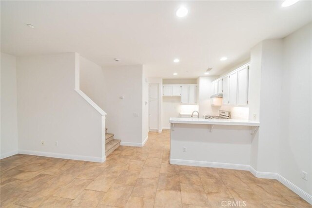 kitchen featuring white cabinetry, kitchen peninsula, a kitchen breakfast bar, stove, and sink