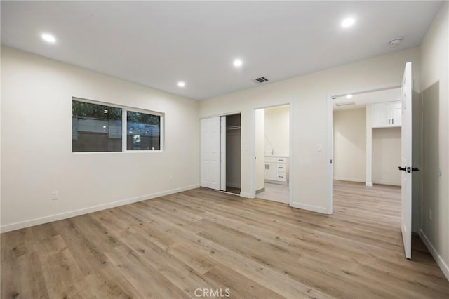 unfurnished bedroom featuring ensuite bathroom, a closet, and light hardwood / wood-style floors