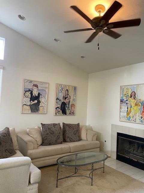 carpeted living room featuring a tiled fireplace, ceiling fan, and vaulted ceiling