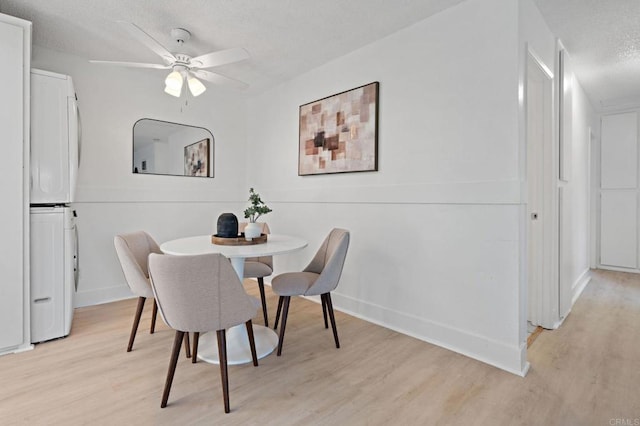 dining room featuring stacked washer / dryer, light wood-style floors, ceiling fan, a textured ceiling, and baseboards