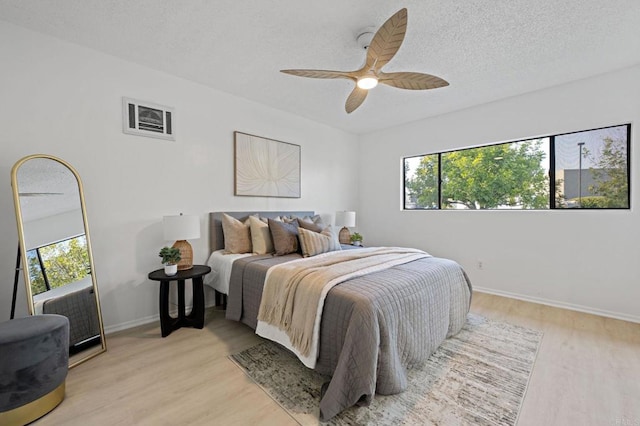 bedroom with multiple windows, light wood-style floors, baseboards, a textured ceiling, and a ceiling fan