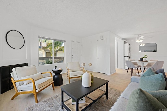living room featuring light wood finished floors, a textured ceiling, and ceiling fan