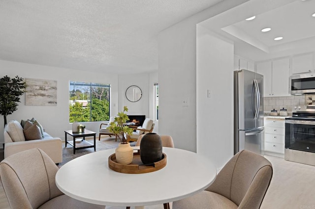 dining area with a warm lit fireplace, light wood-style floors, recessed lighting, and a textured ceiling