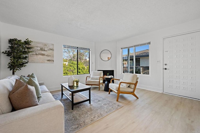 living area featuring a textured ceiling, light wood finished floors, and baseboards