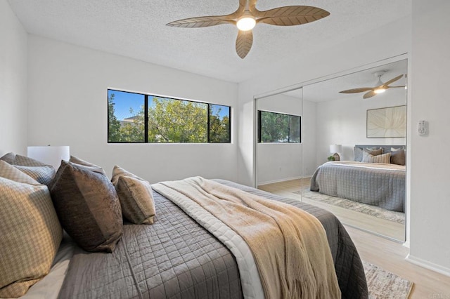 bedroom featuring a textured ceiling, light wood finished floors, a ceiling fan, baseboards, and a closet
