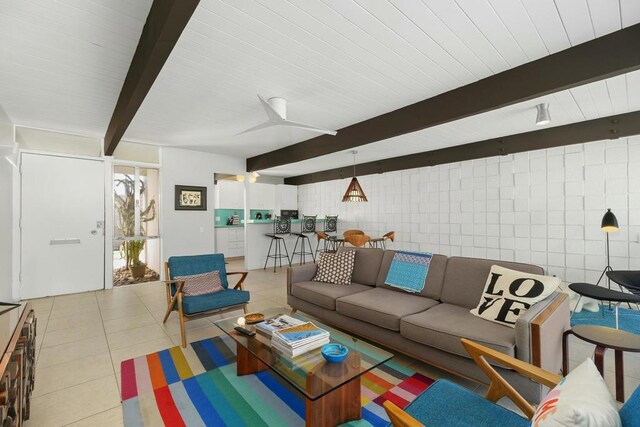 living room featuring light tile patterned floors, beamed ceiling, and tile walls