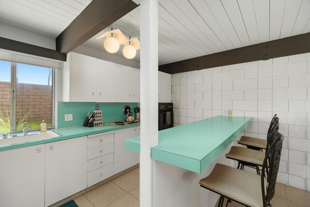 kitchen featuring white cabinetry, sink, beamed ceiling, oven, and a kitchen bar