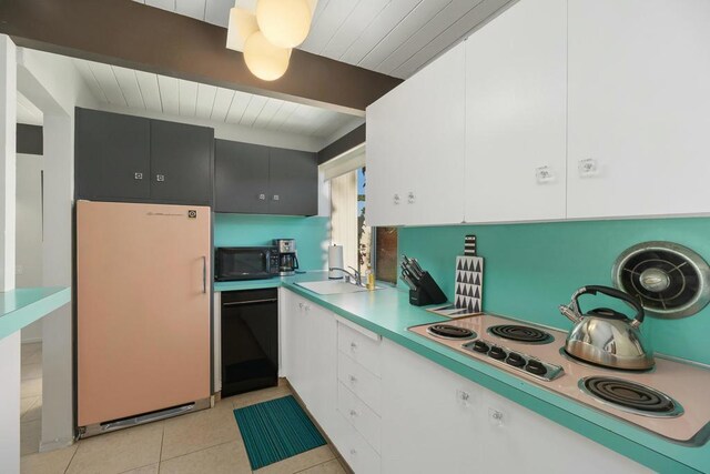 kitchen featuring black appliances, sink, beam ceiling, light tile patterned flooring, and white cabinetry