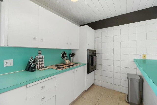 kitchen with white cabinets, black oven, white stovetop, and light tile patterned floors