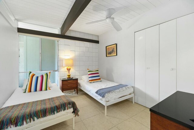 bedroom featuring beam ceiling, ceiling fan, a closet, light tile patterned floors, and tile walls