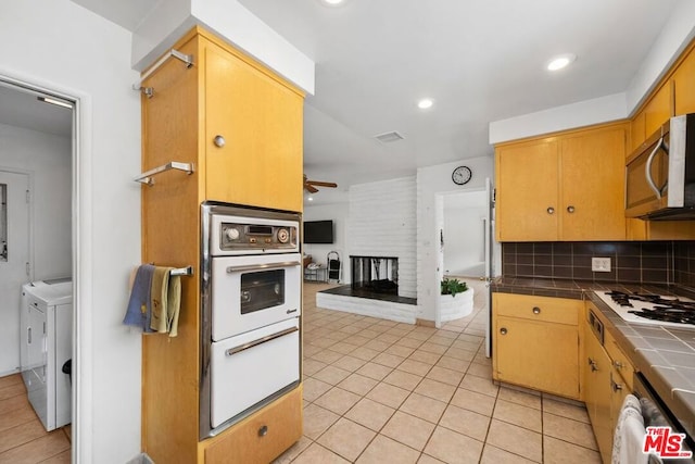 kitchen featuring tasteful backsplash, stainless steel appliances, washing machine and clothes dryer, a fireplace, and tile counters